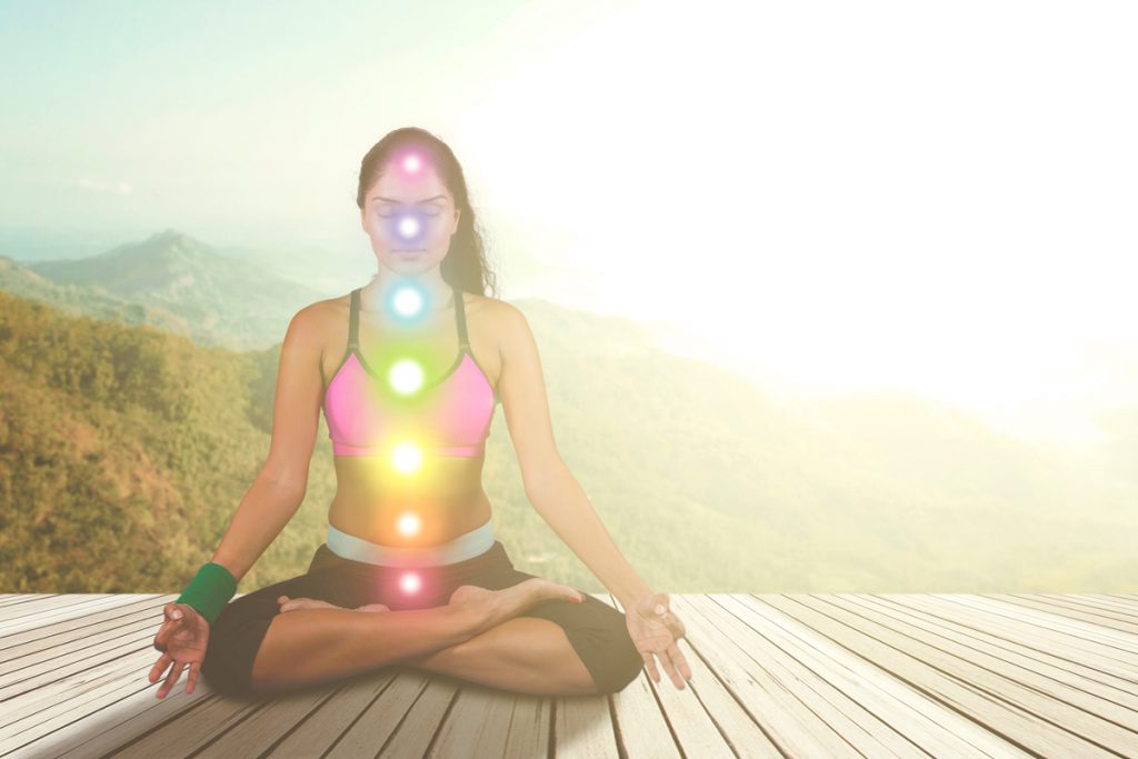 Women meditating in front of sunset, with glowing lights indicating to her chakras
